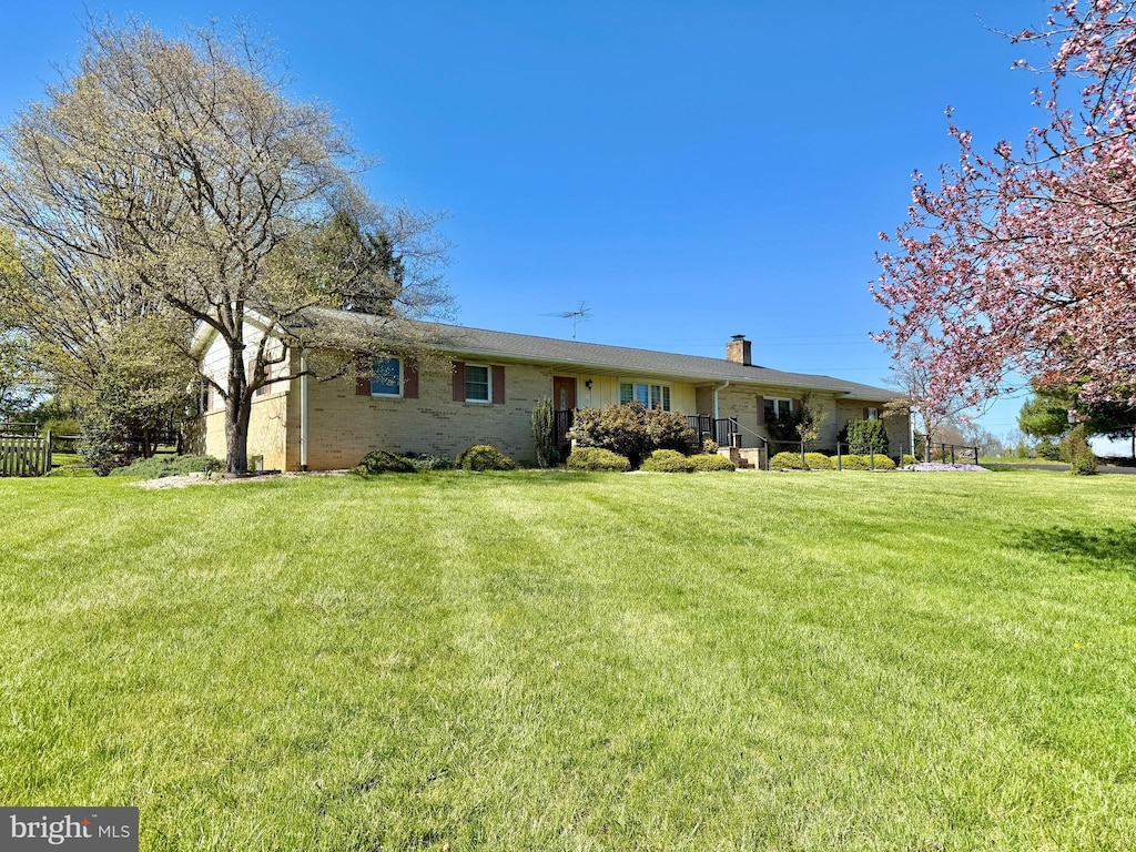 ranch-style house with a chimney, brick siding, and a front yard
