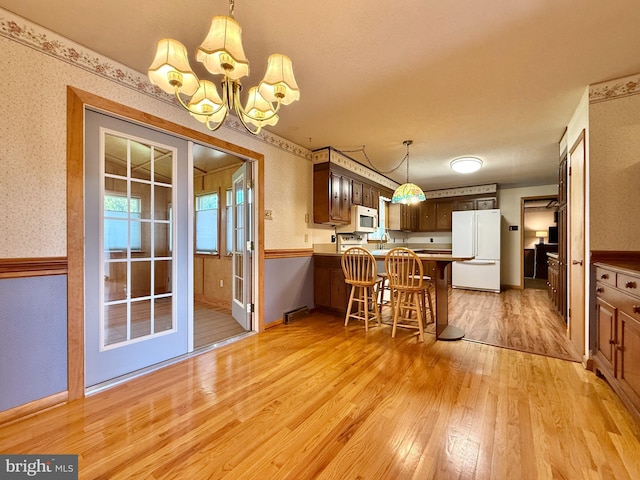 kitchen with a peninsula, white appliances, wallpapered walls, light wood-type flooring, and a notable chandelier