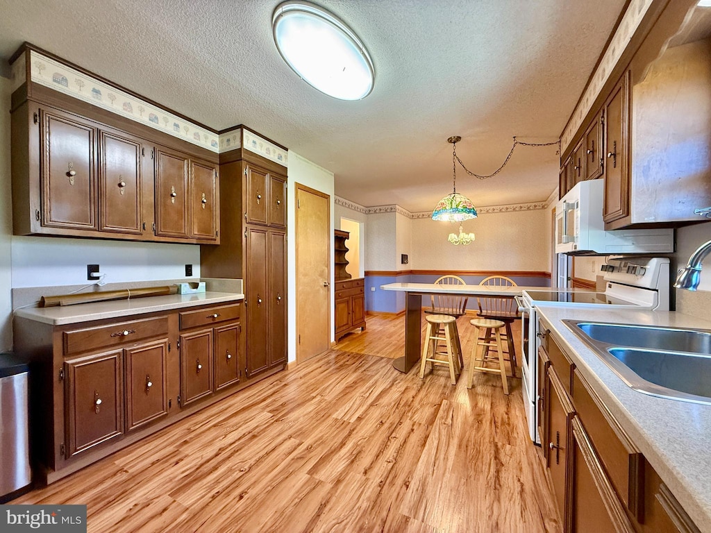kitchen featuring light countertops, light wood-style flooring, hanging light fixtures, and white appliances