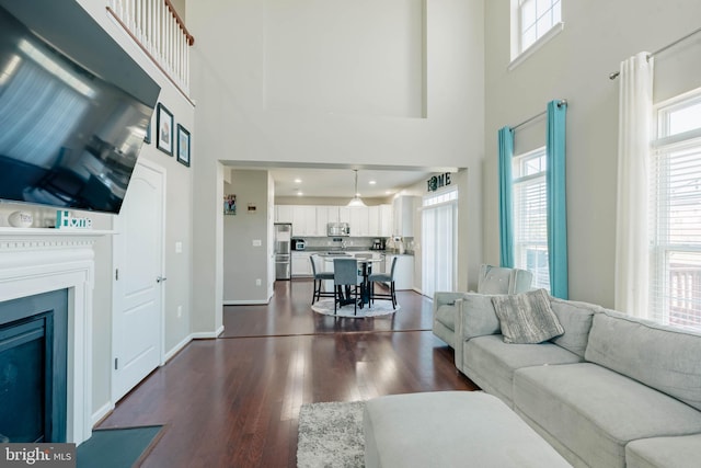living area featuring a healthy amount of sunlight, a high ceiling, dark wood-style flooring, and a fireplace with flush hearth