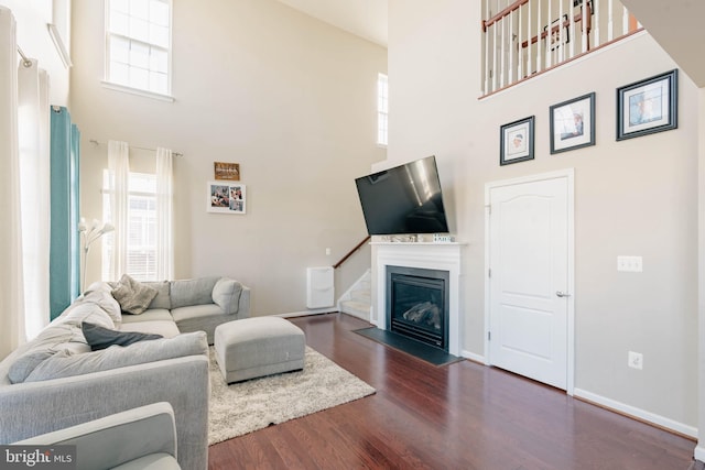 living area featuring dark wood-type flooring, a fireplace with flush hearth, and a towering ceiling