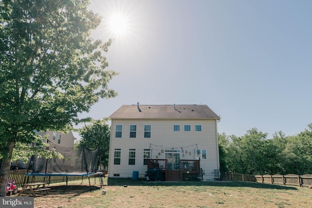 back of house with a wooden deck, fence, a trampoline, and a yard