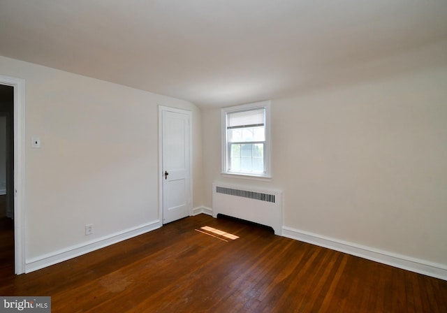 unfurnished room with dark wood-type flooring, baseboards, and radiator