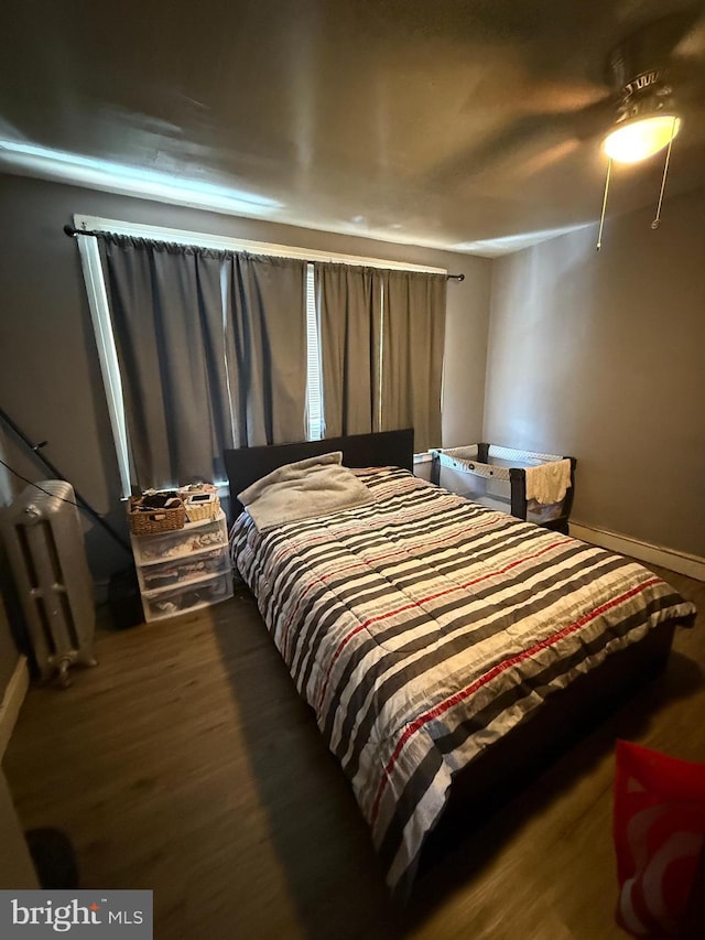 bedroom with radiator, wood finished floors, and baseboards