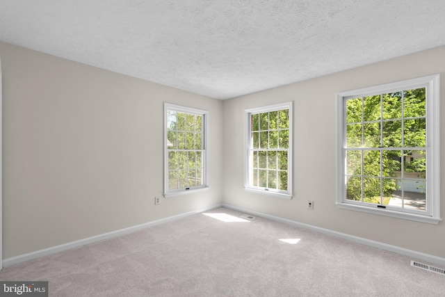 carpeted empty room with a textured ceiling, baseboards, and visible vents