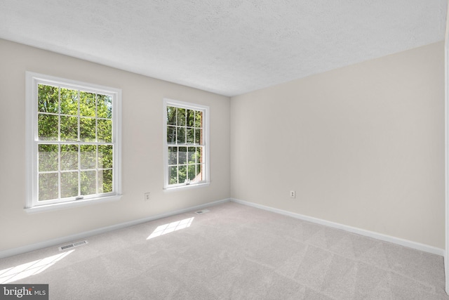 empty room featuring carpet flooring, a textured ceiling, baseboards, and visible vents