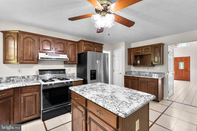 kitchen featuring a ceiling fan, light tile patterned floors, stainless steel fridge with ice dispenser, range with gas stovetop, and under cabinet range hood