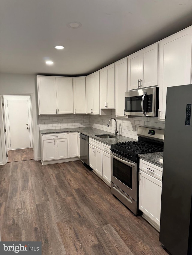 kitchen featuring white cabinetry, decorative backsplash, a sink, appliances with stainless steel finishes, and dark wood-type flooring