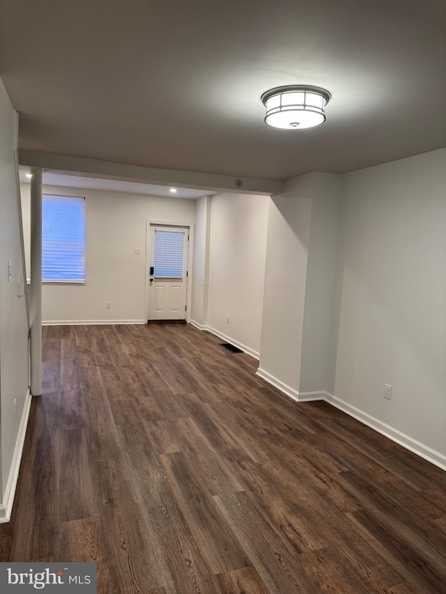 empty room with dark wood-type flooring, visible vents, and baseboards