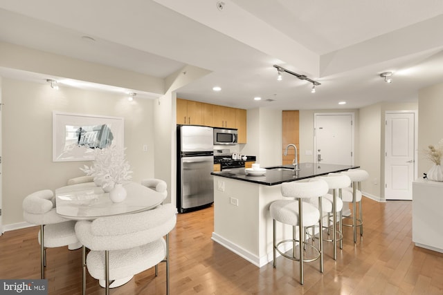 kitchen with light wood-style flooring, appliances with stainless steel finishes, dark countertops, a sink, and a kitchen breakfast bar