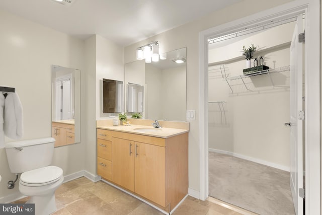 bathroom with toilet, a spacious closet, vanity, and baseboards