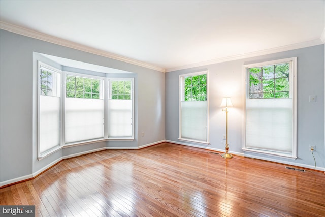 empty room featuring hardwood / wood-style flooring, ornamental molding, and baseboards