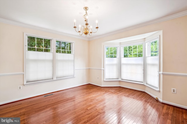 unfurnished room featuring a chandelier, plenty of natural light, wood-type flooring, baseboards, and crown molding