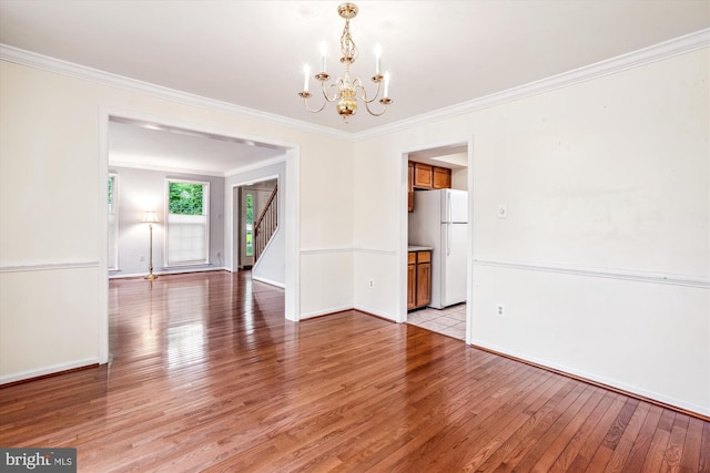 empty room featuring a chandelier, light wood-type flooring, stairway, baseboards, and crown molding