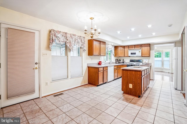 kitchen with white appliances, light countertops, brown cabinetry, a chandelier, and a center island