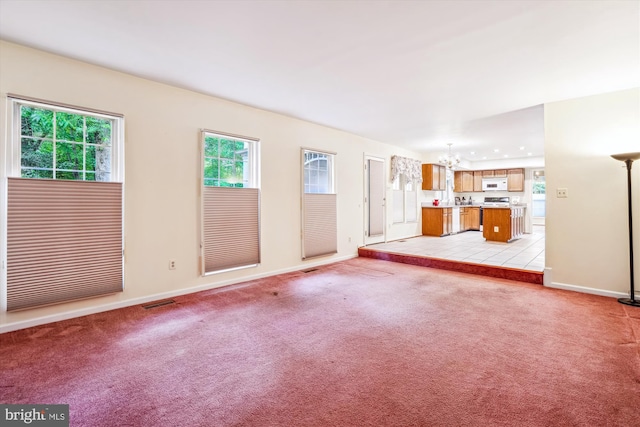 unfurnished living room featuring a chandelier, baseboards, and light carpet