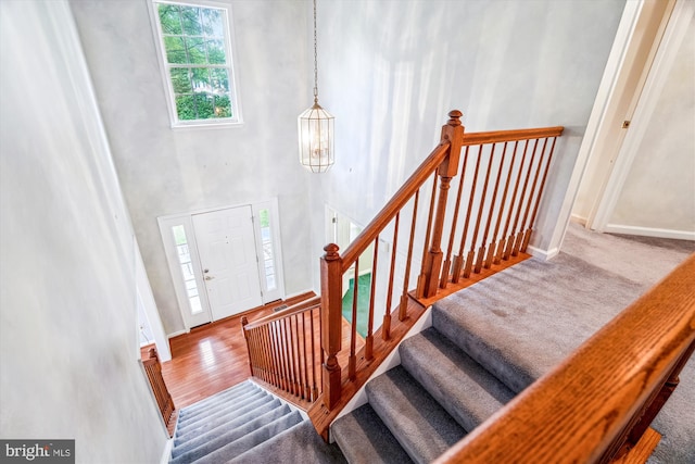 foyer entrance with a high ceiling, baseboards, stairway, carpet, and a chandelier