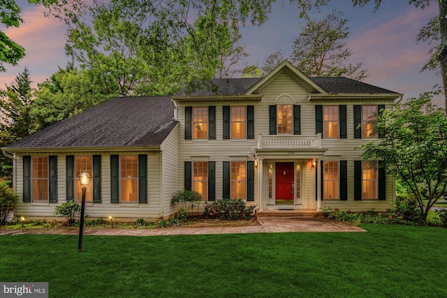 colonial-style house featuring a lawn and roof with shingles