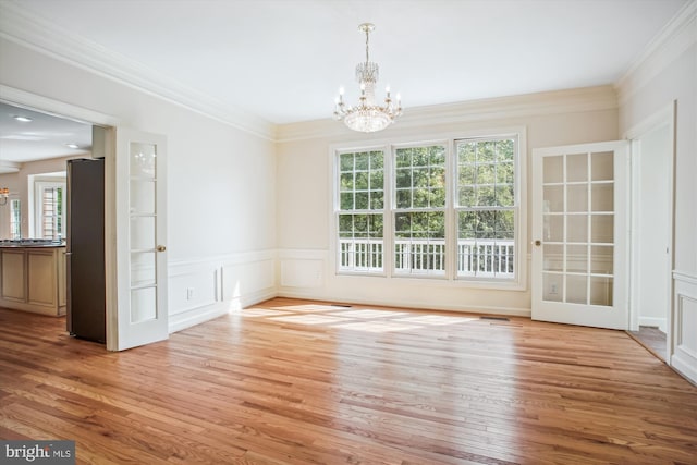 unfurnished dining area featuring ornamental molding, a chandelier, plenty of natural light, and wood finished floors