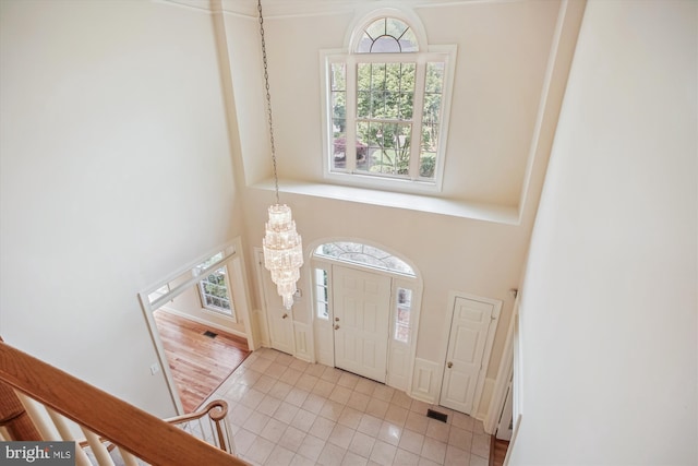 entrance foyer with an inviting chandelier, a towering ceiling, light tile patterned floors, and visible vents