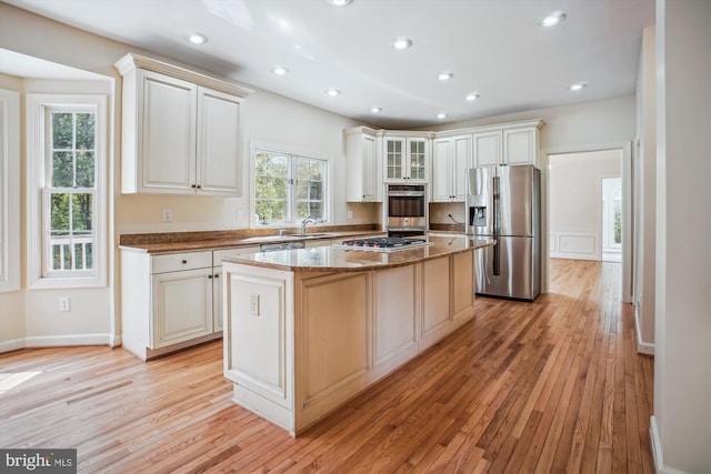 kitchen featuring a sink, light wood-style floors, stone countertops, stainless steel appliances, and a kitchen island