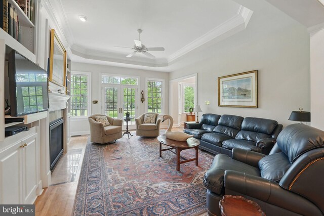 living area with crown molding, ceiling fan, light wood finished floors, a high end fireplace, and a tray ceiling