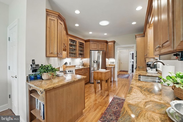 kitchen with light stone countertops, stainless steel fridge, a sink, and light wood-style flooring