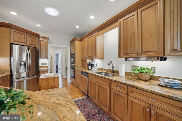 kitchen with a sink, paneled dishwasher, brown cabinetry, and stainless steel refrigerator with ice dispenser