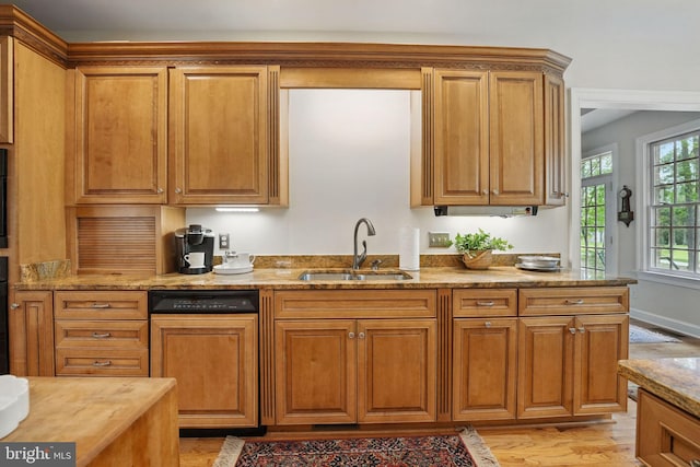kitchen featuring light stone counters, a sink, light wood-style floors, brown cabinetry, and paneled dishwasher