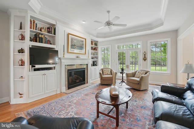 living area featuring crown molding, built in features, light wood-style flooring, a ceiling fan, and a fireplace with flush hearth