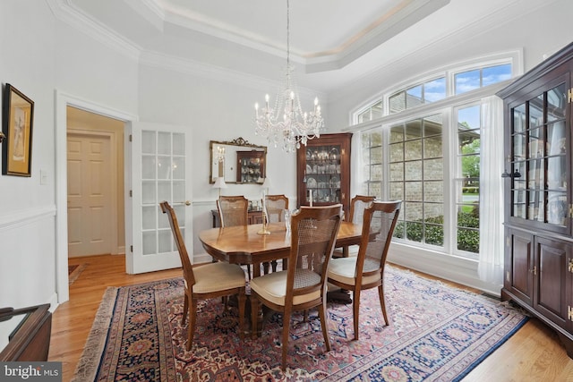 dining room featuring crown molding, a raised ceiling, light wood finished floors, and a chandelier