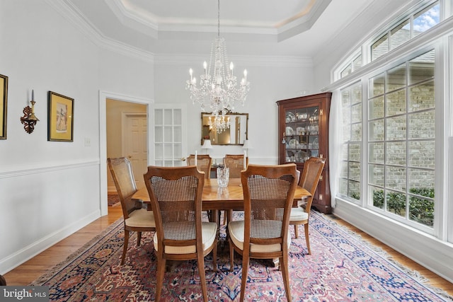 dining space with a healthy amount of sunlight, a raised ceiling, an inviting chandelier, and wood finished floors