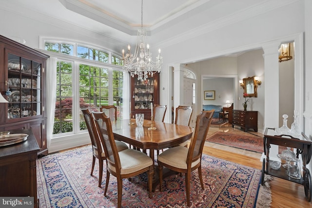 dining room with light wood finished floors, a tray ceiling, a notable chandelier, and a healthy amount of sunlight