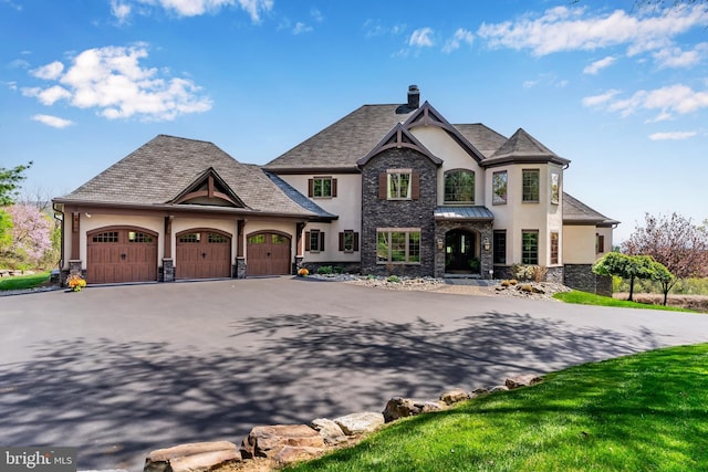 french country style house featuring a garage, stone siding, stucco siding, a chimney, and driveway