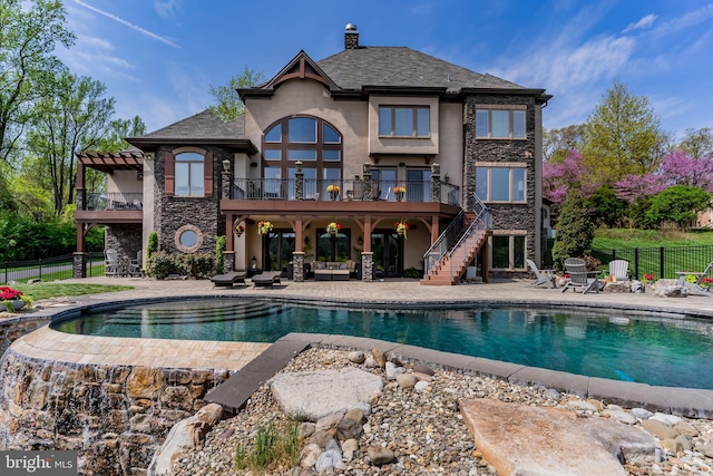 rear view of house with a patio area, stairway, fence, stone siding, and stucco siding