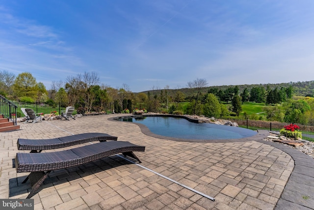 view of swimming pool with a patio, a fenced in pool, fence, and a forest view