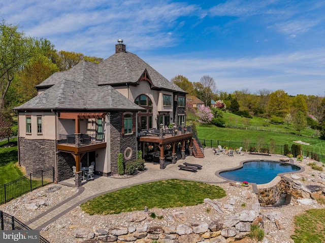 rear view of house with stone siding, stucco siding, a deck, a fenced backyard, and a patio