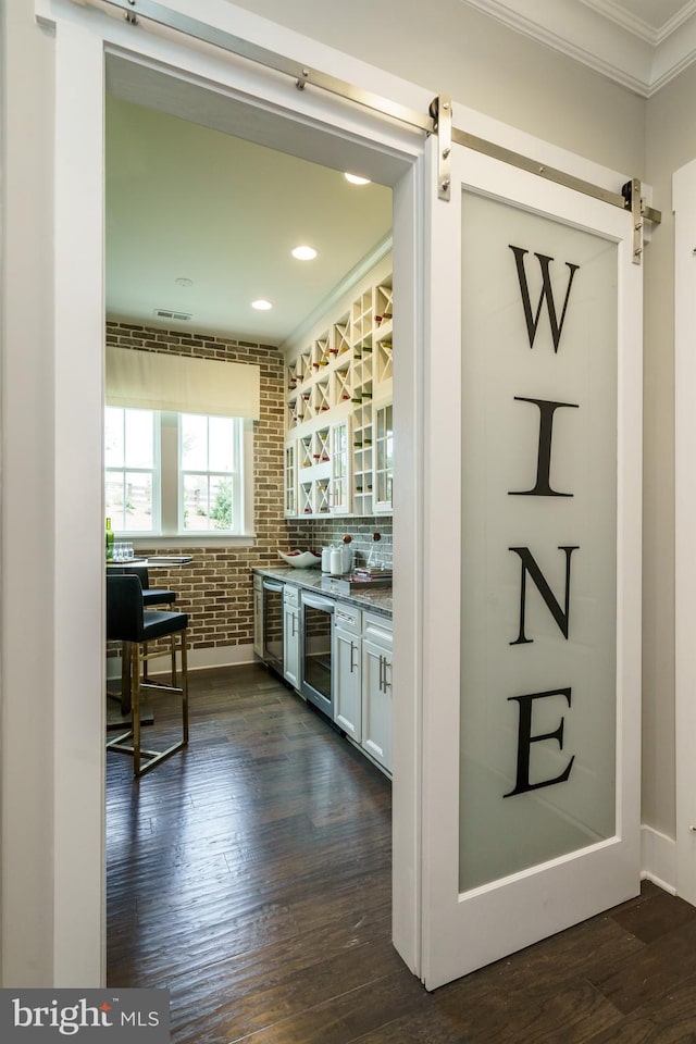 bar featuring crown molding, dark wood-style flooring, a barn door, and beverage cooler