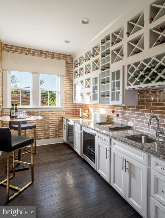 kitchen with light stone countertops, a sink, brick wall, glass insert cabinets, and wine cooler