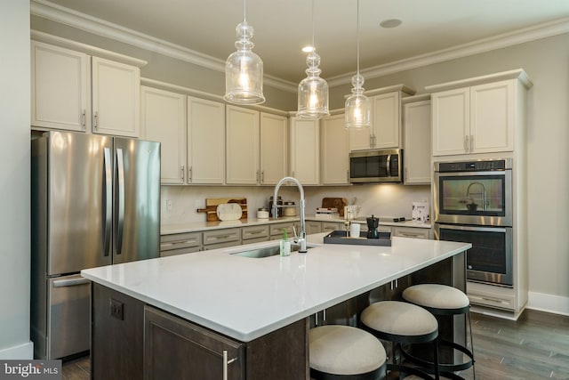kitchen with a sink, dark wood-style flooring, stainless steel appliances, a center island with sink, and light countertops
