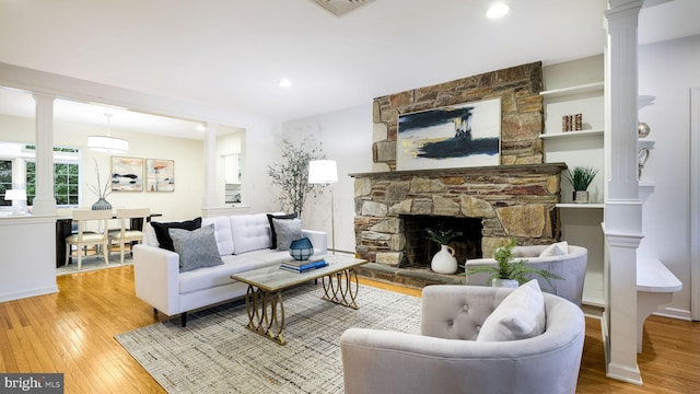 living area featuring ornate columns, wood-type flooring, and a stone fireplace