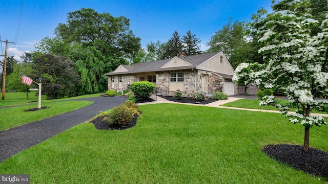 view of front of property with stone siding, a front lawn, an attached garage, and driveway