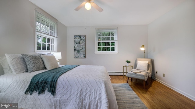 bedroom with a baseboard heating unit, wood finished floors, baseboards, and ceiling fan