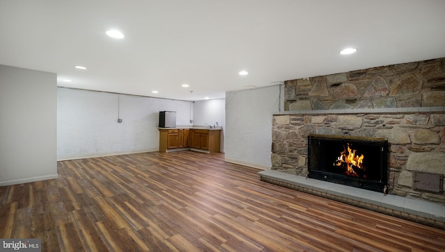 unfurnished living room featuring wood finished floors, recessed lighting, a fireplace, bar, and baseboards