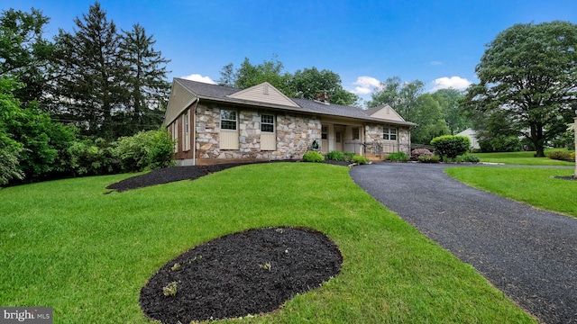 ranch-style house with stone siding, a front yard, a chimney, and asphalt driveway