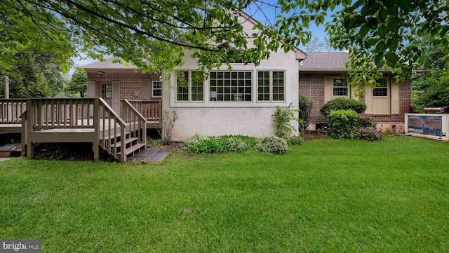 rear view of property featuring brick siding, a yard, a wooden deck, and roof with shingles