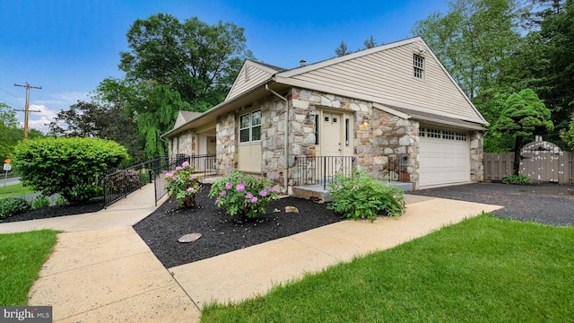 view of front of property featuring stone siding, asphalt driveway, and fence