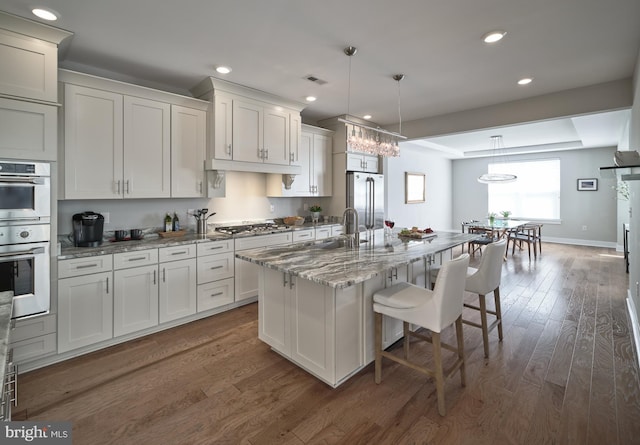 kitchen featuring light stone countertops, a kitchen breakfast bar, wood finished floors, a center island with sink, and appliances with stainless steel finishes