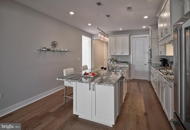 kitchen with a sink, a breakfast bar, visible vents, a center island with sink, and dark wood-style floors