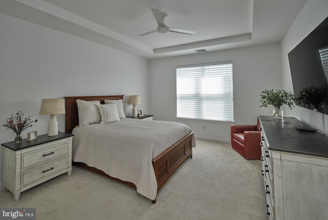 bedroom with a ceiling fan, a tray ceiling, baseboards, visible vents, and light colored carpet
